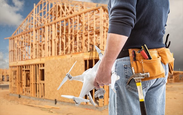 Construction worker and drone pilot with toolbelt holding drone at construction site