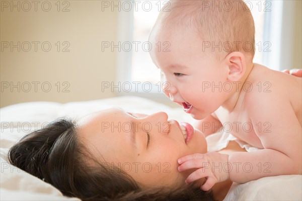 Young mixed-race chinese and caucasian baby boy laying in his bed with his mother