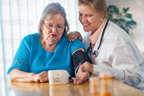 Senior adult woman learning from female doctor to use blood pressure machine