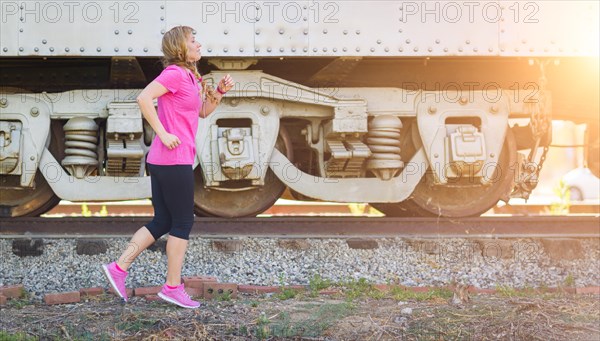 Young fit adult woman outdoors during workout listening to music with earphones near train and tracks