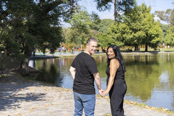 Multi-ethnic couple formed by an Andean woman and a Caucasian man walking by a lake. Happy expressions and faces of lovers