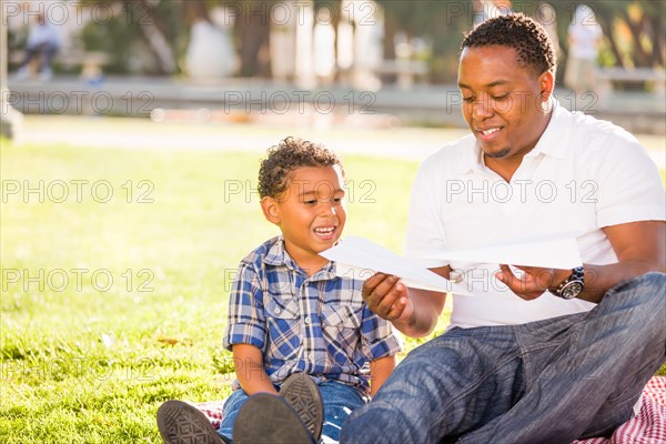 Happy african american father and mixed-race son playing with paper airplanes in the park