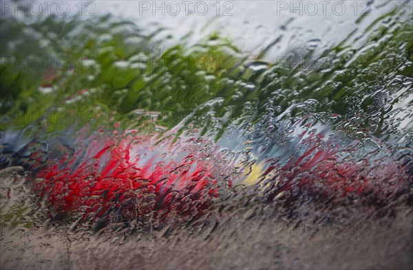 Blick durch eine nasse Windschutzscheibe auf geparkte Autos am Parkplatz