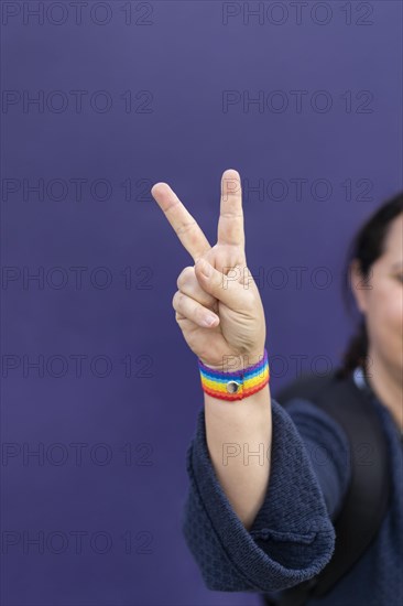 Detail of arm and hand of woman wearing gay wristband on purple background