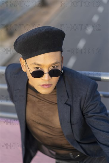 Latino gay male with makeup wearing trendy hat posing on a bridge