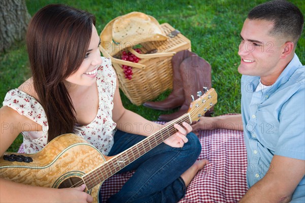 Young adult girl playing guitar with boyfriend in the park