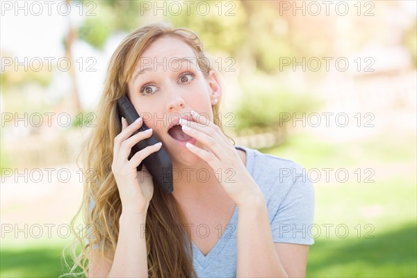 Stunned young woman outdoors talking on her smart phone