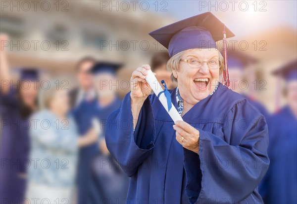 Happy senior woman in hat and gown at outdoor graduation ceremony