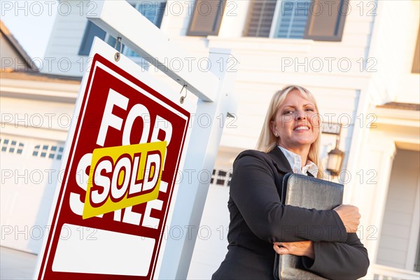 Female real estate agent in front of sold for sale sign and beautiful house