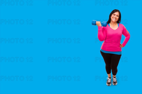 Middle aged hispanic woman in workout clothes holding dumbbell against A bright cyan blue background