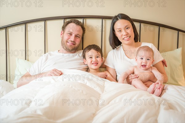 Young mixed-race chinese and caucasian baby boys laying in bed with their father and mother