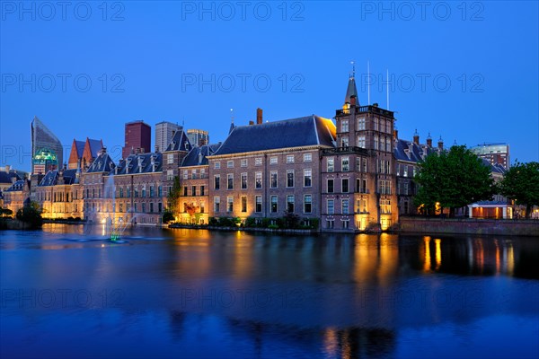 View of the Binnenhof House of Parliament and the Hofvijver lake with downtown skyscrapers in background illuminated in the evening