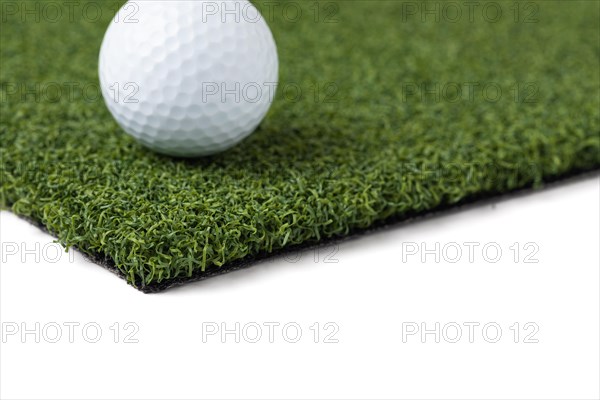 Golf ball resting on section of artificial turf grass on white background