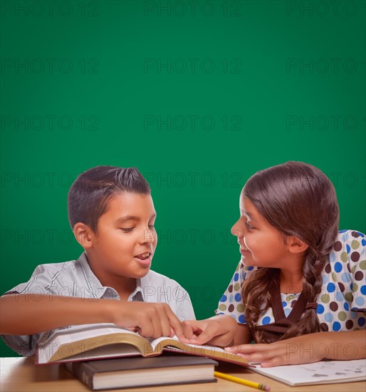 Blank chalk board behind hispanic boy and girl having fun studying together