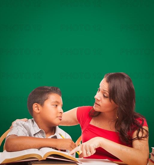 Blank chalk board behind hispanic young boy and famale adult studying