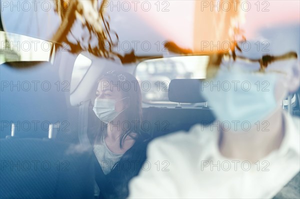 A woman wearing a protective mask sitting on the back seat of a taxi car