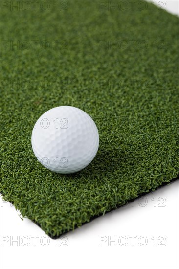 Golf ball resting on section of artificial turf grass on white background