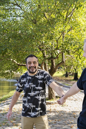 Gay man surprised and happy because his boyfriend holds his hand in public while they are walking in a lake. Coming out concept