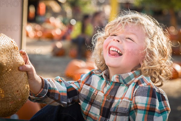 Little boy sitting with A cowboy hat in a rustic ranch setting at the pumpkin patch