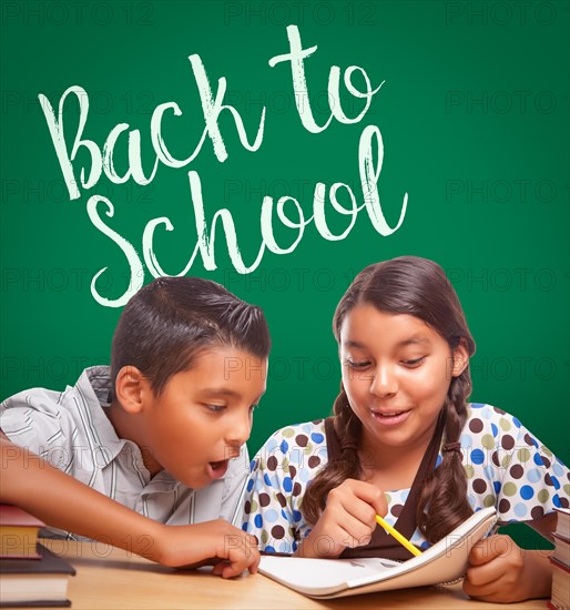 Back to school written on chalk board behind hispanic boy and girl having fun studying together