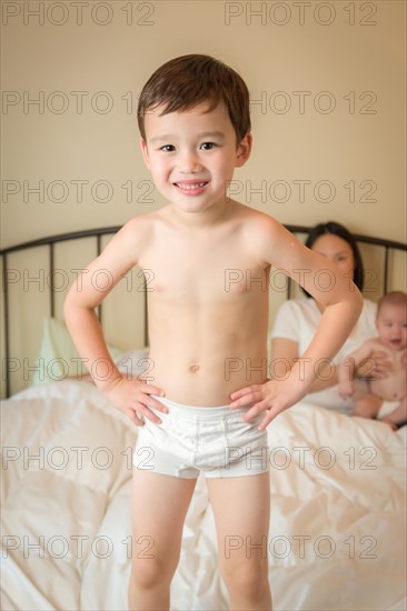 Young mixed-race chinese and caucasian boy jumping in bed with his family