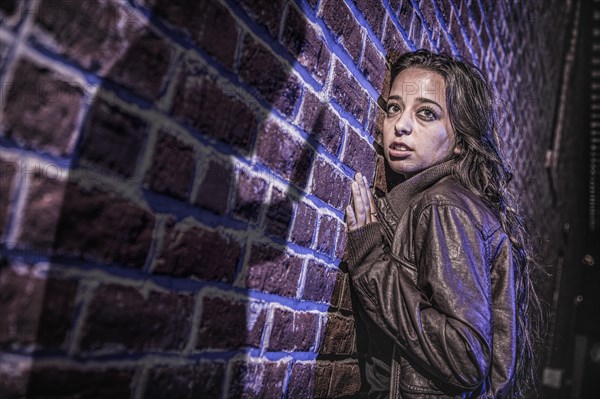 Male shadow figure with knife threatens frightened young woman against brick wall