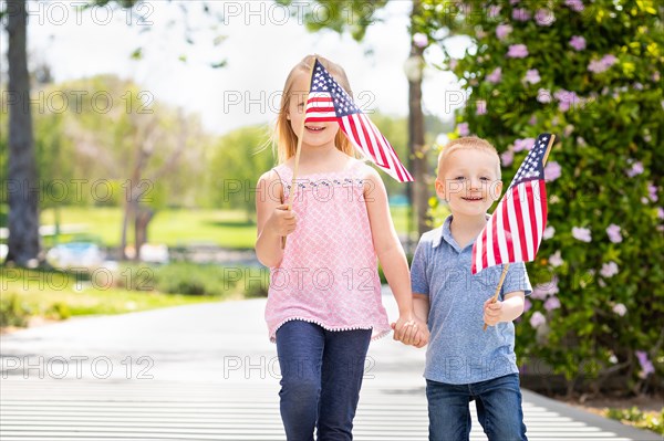 Young sister and brother waving american flags at the park