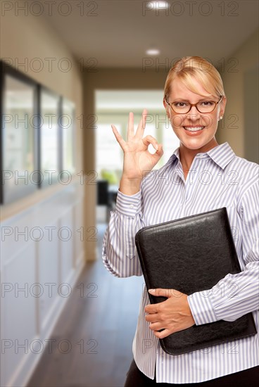 Smiling businesswoman with folder and okay hand sign in hallway of house