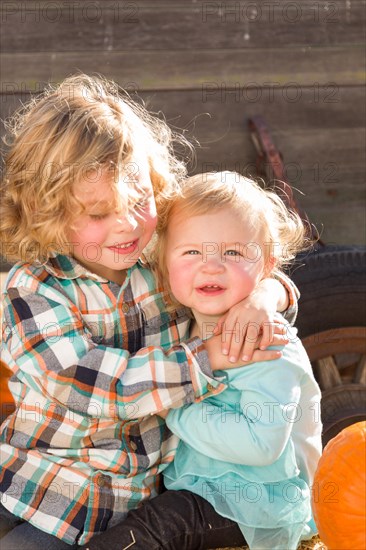 Sweet little boy plays with his baby sister in a rustic ranch setting at the pumpkin patch