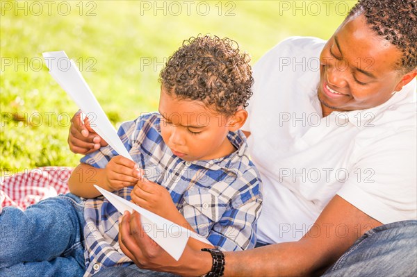 Happy african american father and mixed-race son playing with paper airplanes in the park