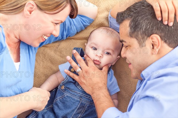 Young mixed-race couple laying with their infant on A blanket