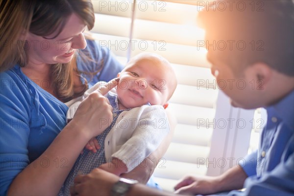 Happy mixed-race couple enjoying their newborn son in the light of the window