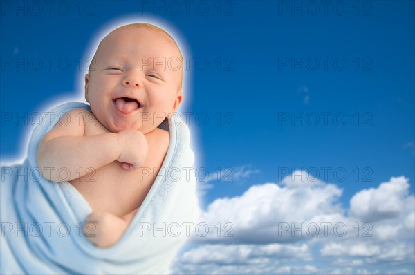 Beautiful laughing baby boy wrapped in his blanket with A blue sky background