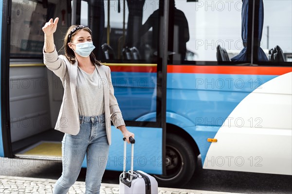 A young woman with mask and luggage has just left the bus after a long trip