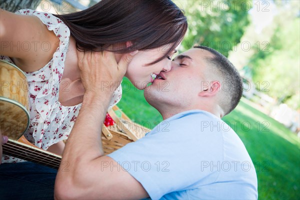 Young adult couple with guitar kissing in the park