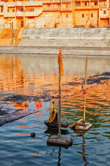Lingam religious symbol representation of the Hindu deity Shiva decorated with flower garland used for worship in Kshipra river