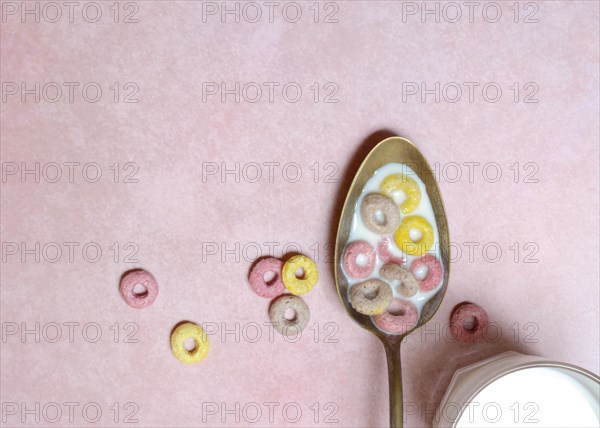 Fruit-flavoured cereal rings in spoon and glass of milk