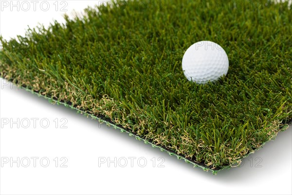 Golf ball resting on section of artificial turf grass on white background