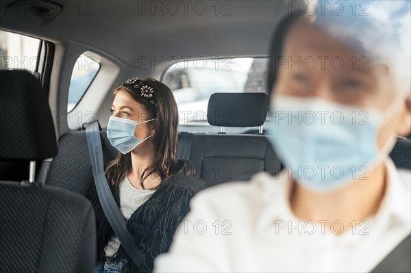 A woman wearing a protective mask sitting on the back seat of a taxi car