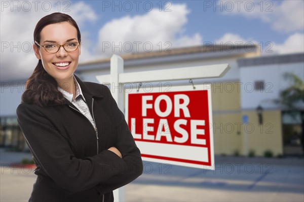 Attractive serious mixed-race woman in front of vacant retail building and for lease real estate sign