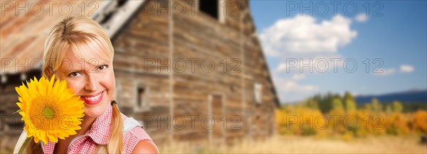 Beautiful caucasian young woman holding sunflower in front of rustic barn in the country