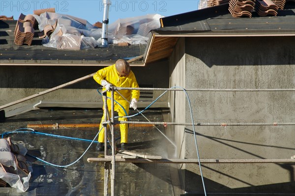 Construction worker pressure washes fresh applied surface of new home exterior