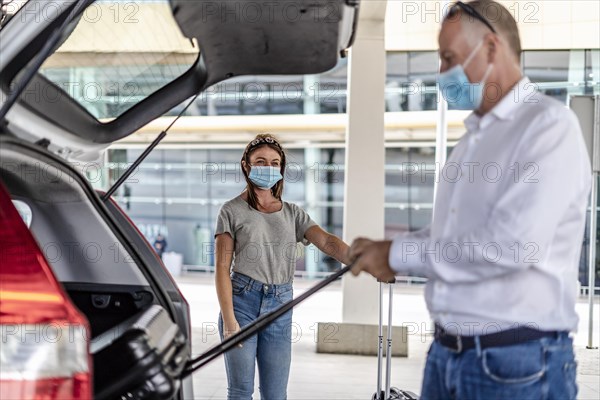 A taxi or Uber driver helping a passenger in a protective mask with her luggage at the airport