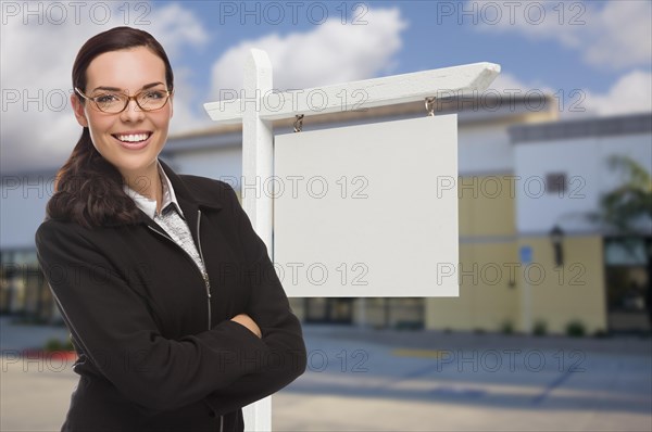Attractive serious mixed-race woman in front of vacant retail building and blank real estate sign