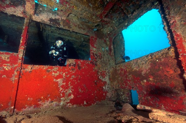 Diver with underwater lamp swims through shipwreck