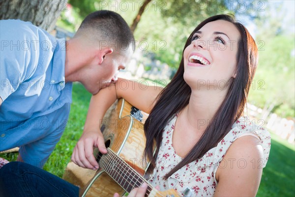 Young adult girl playing guitar with boyfriend in the park