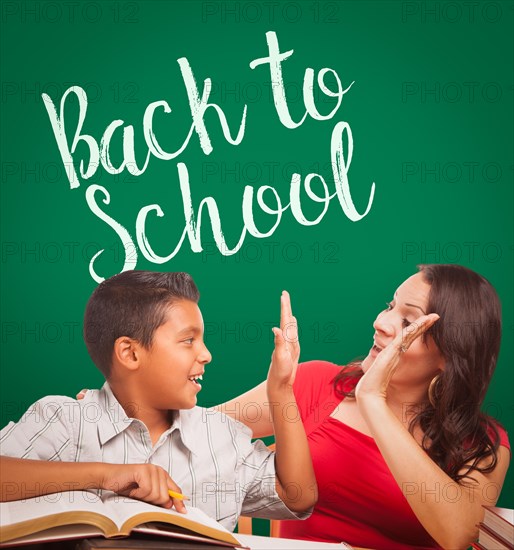 Back to school written on chalk board behind hispanic young boy and famale adult studying