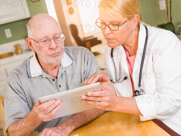 Female doctor or nurse showing senior man touch pad computer at home