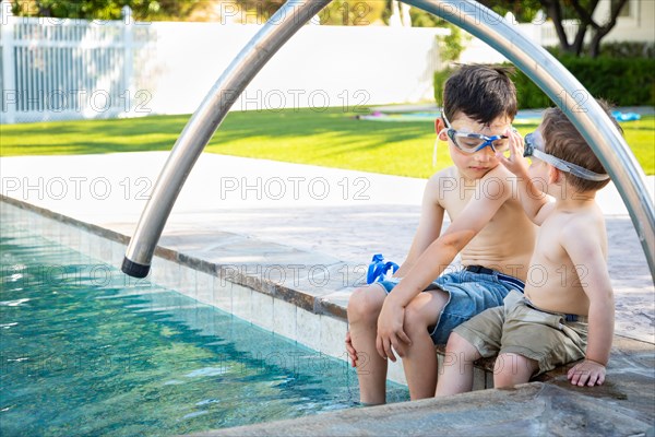 Young mixed-race chinese and caucasian brothers wearing swimming goggles playing at the pool