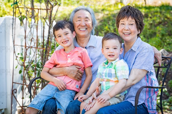 Chinese grandparents and mixed-race children sit on bench outdoors